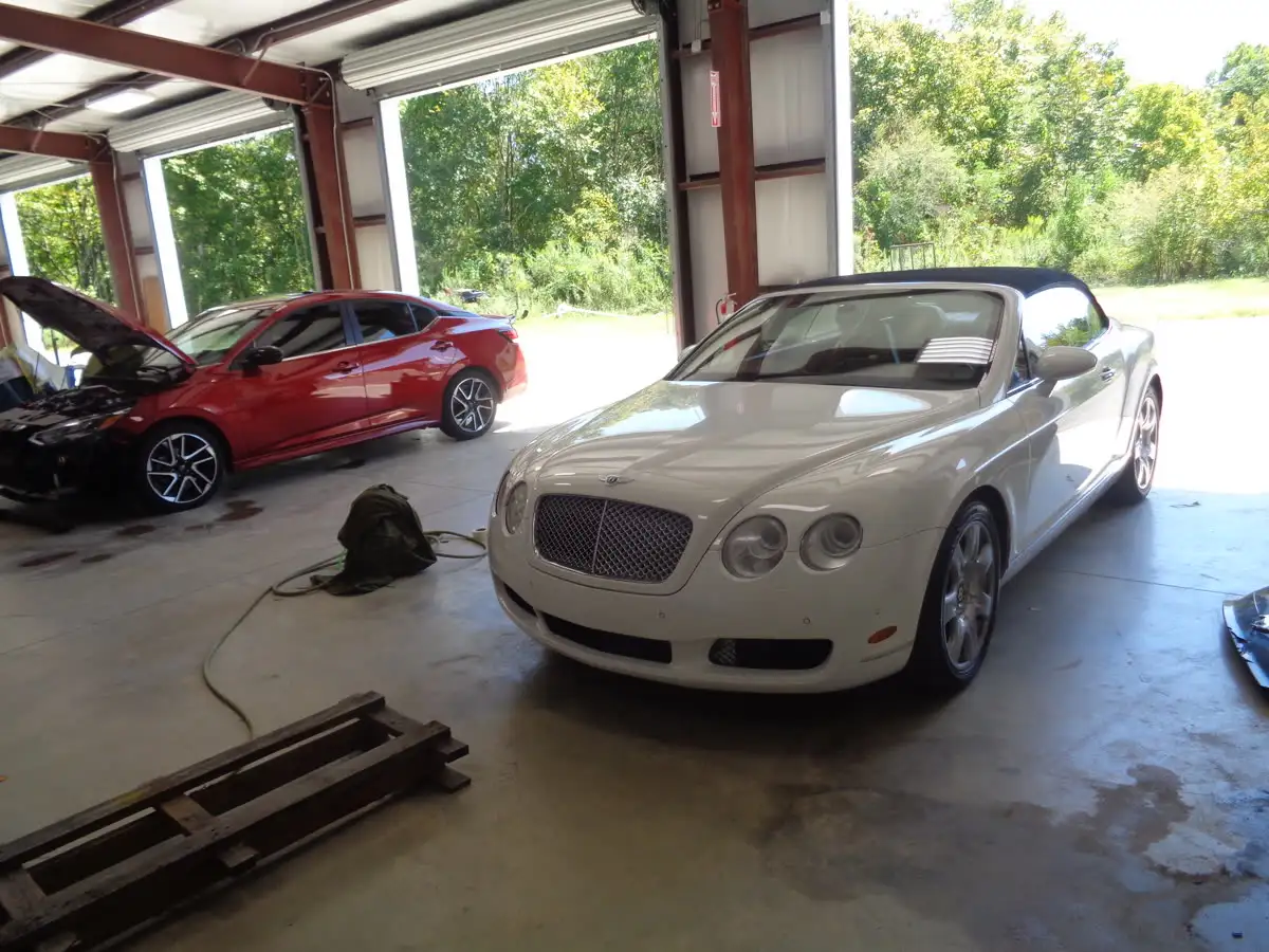 White convertible and red sedan with its hood open in a repair bay at Ron's
